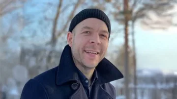 Glad man med sotarmössa och svart jacka , bakom finns det träd